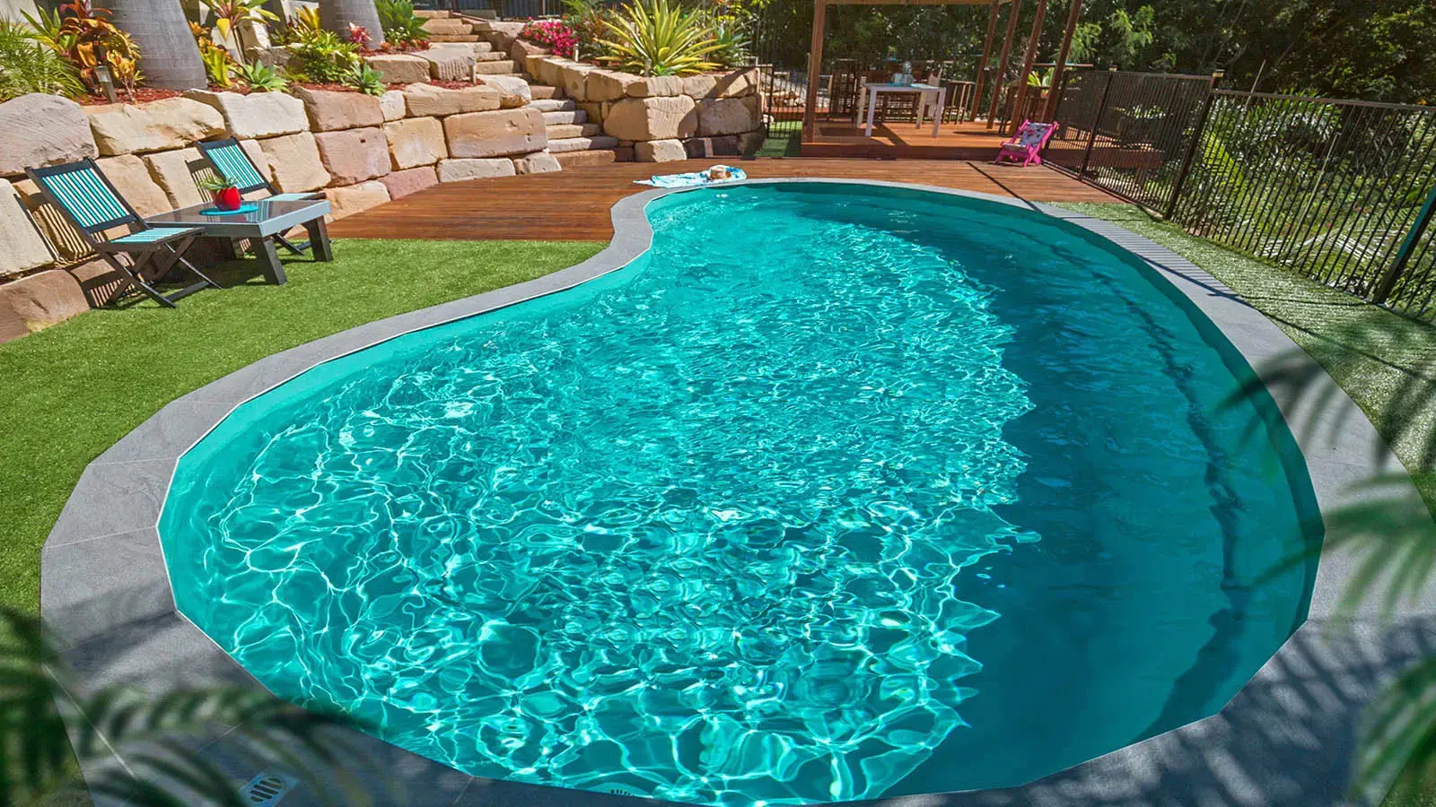Backyard pool with wooden deck and chairs.